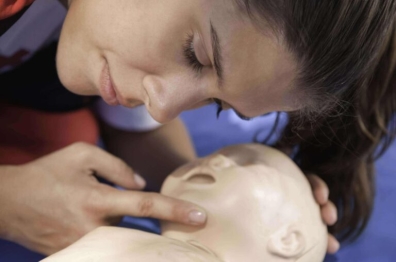 Woman practicing CPR on an infant dummy, checking for breathing and pulse during a first aid training session.