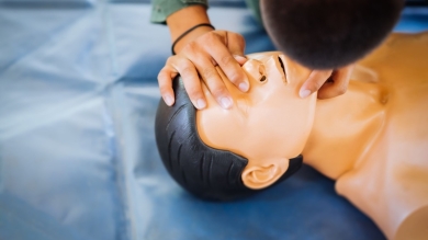 Person practicing CPR rescue breathing on a medical training manikin placed on a blue mat.