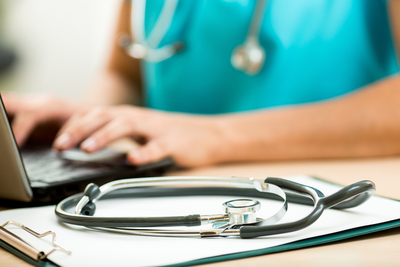 woman working on a laptop with a stethoscope next to her