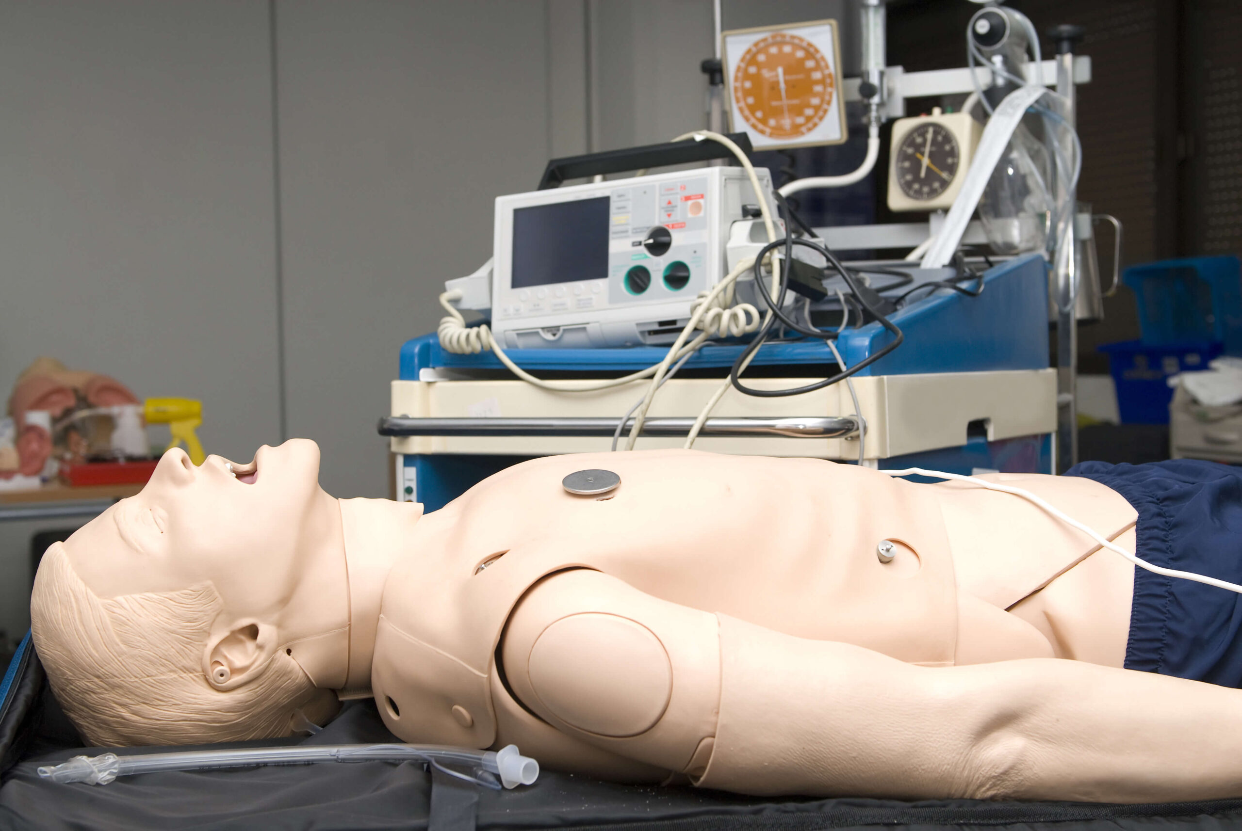 A medical training mannequin lies on an examination bed with equipment.